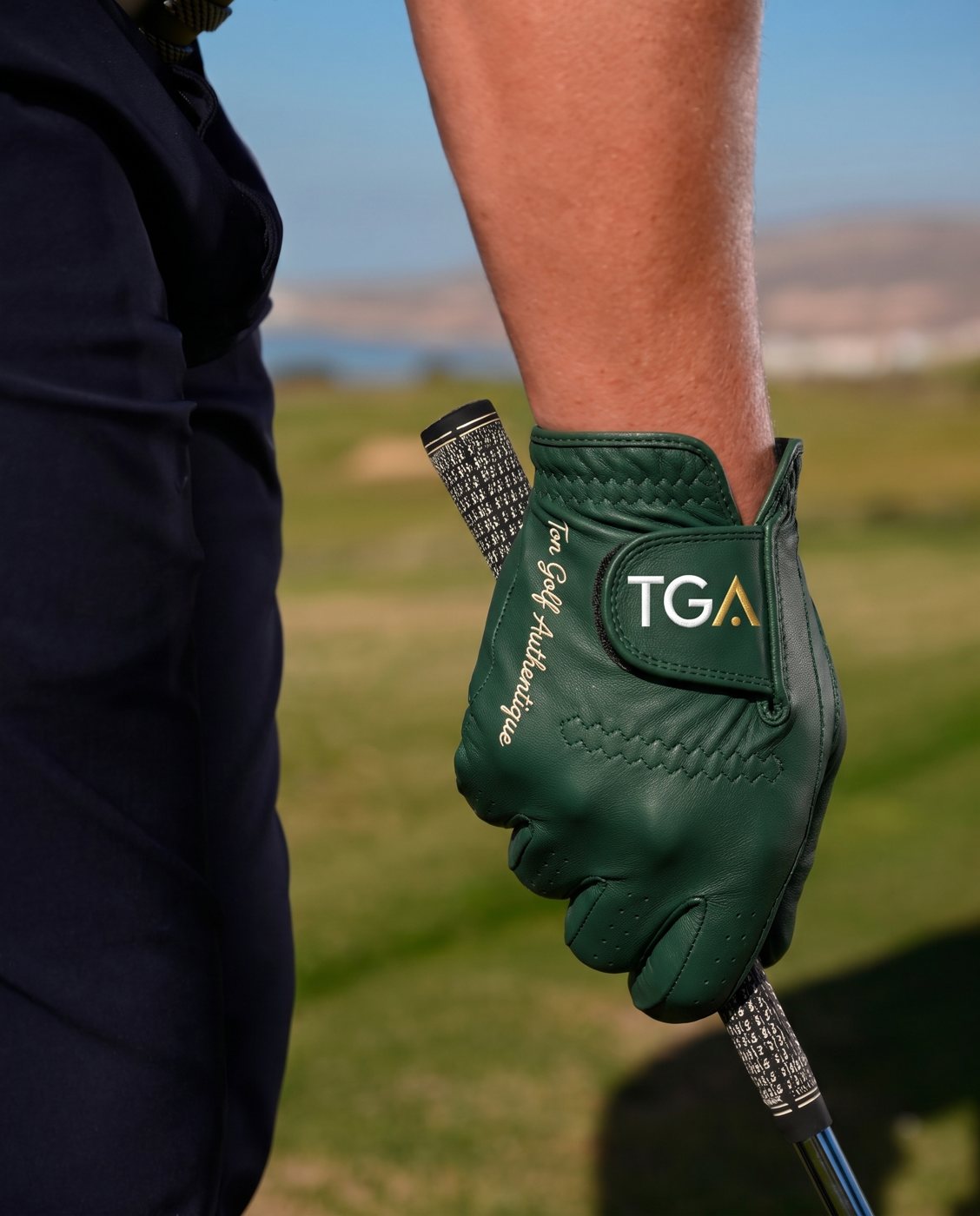 Main gantée de vert sur le grip d'un club, logo TGA